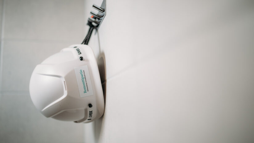 Kuvassa kylpyhuoneen seinän naulakosta roikkuva valkoinen suojakypärä. Kypärässä Remonttipartion logo.